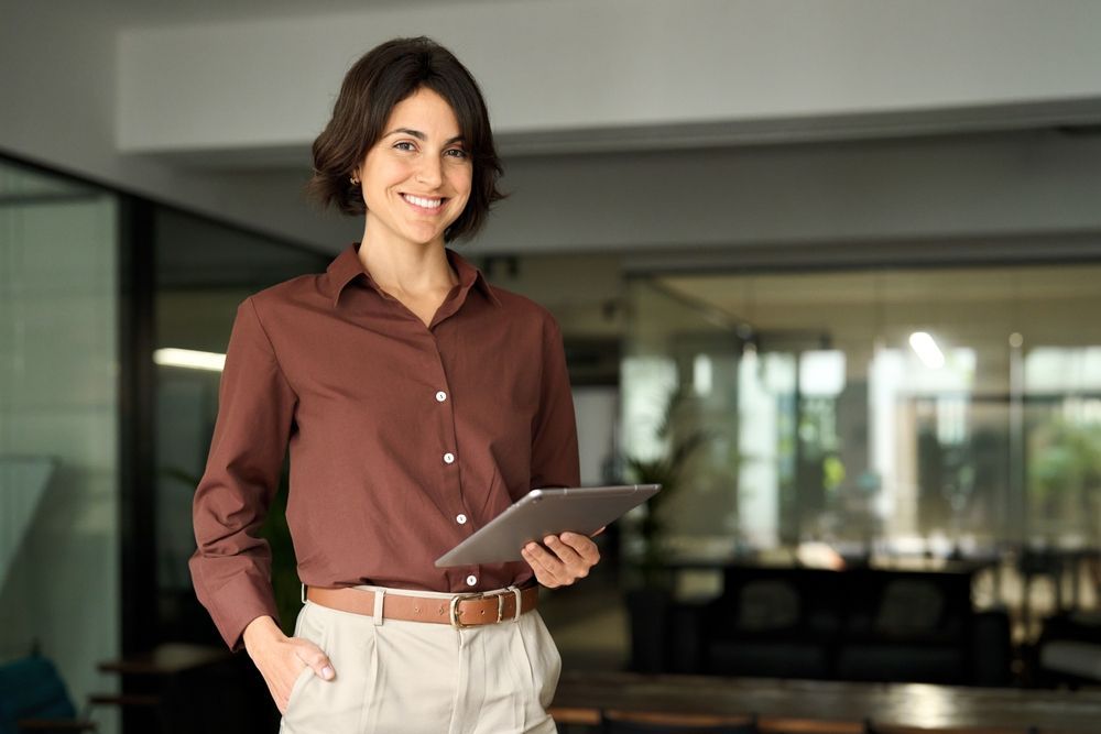 A woman is standing in an office holding a tablet computer.