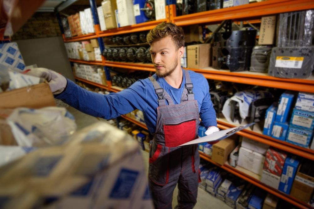 A man is standing in a warehouse looking at a clipboard.
