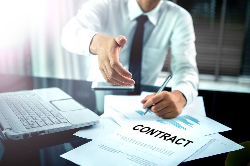 A man is shaking hands with another man while signing a contract.