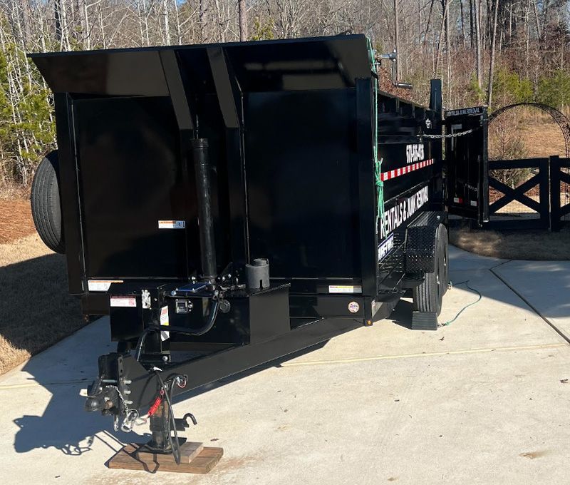 A black dumpster trailer is parked on a concrete driveway.