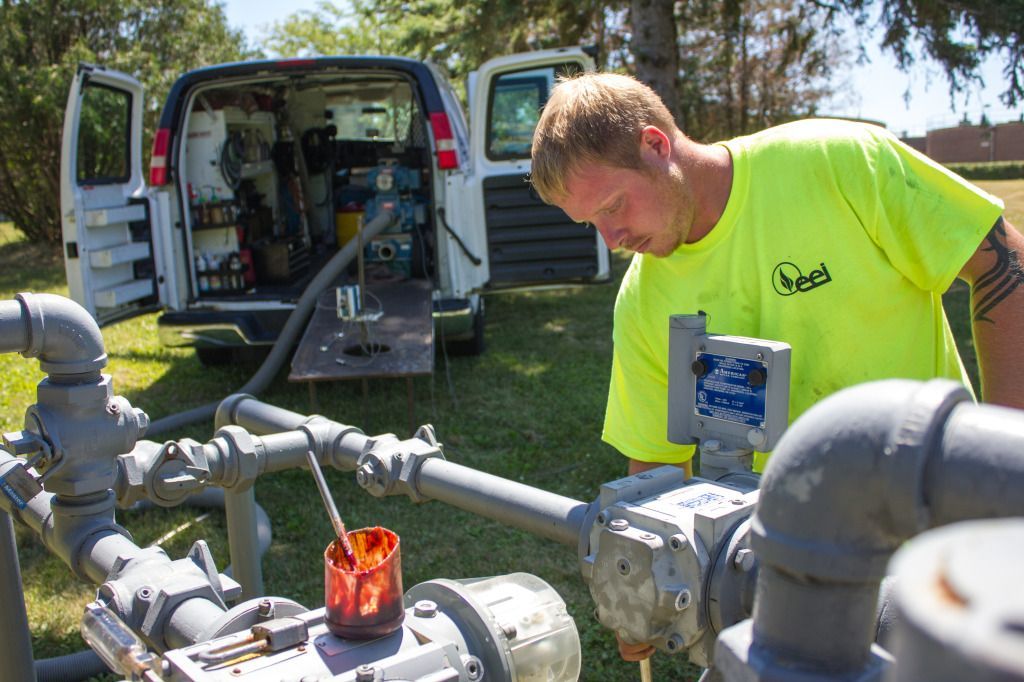 A worker in a neon green shirt performs field testing of a rotary gas meter, with a van in the background.