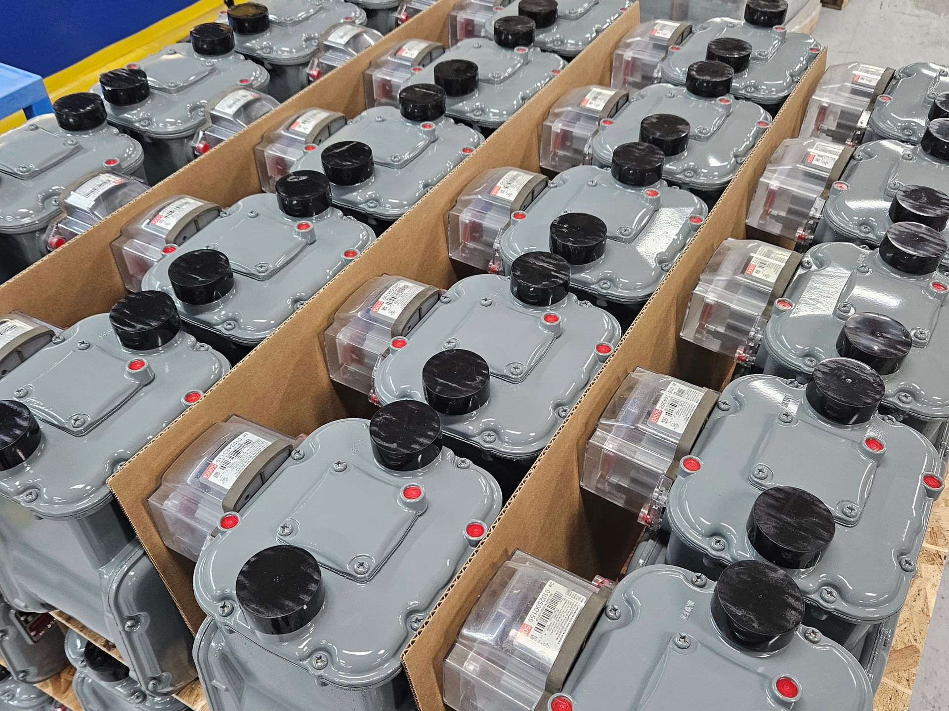 Rows of remanufactured, gray natural gas meters packed in cardboard dividers on a pallet.