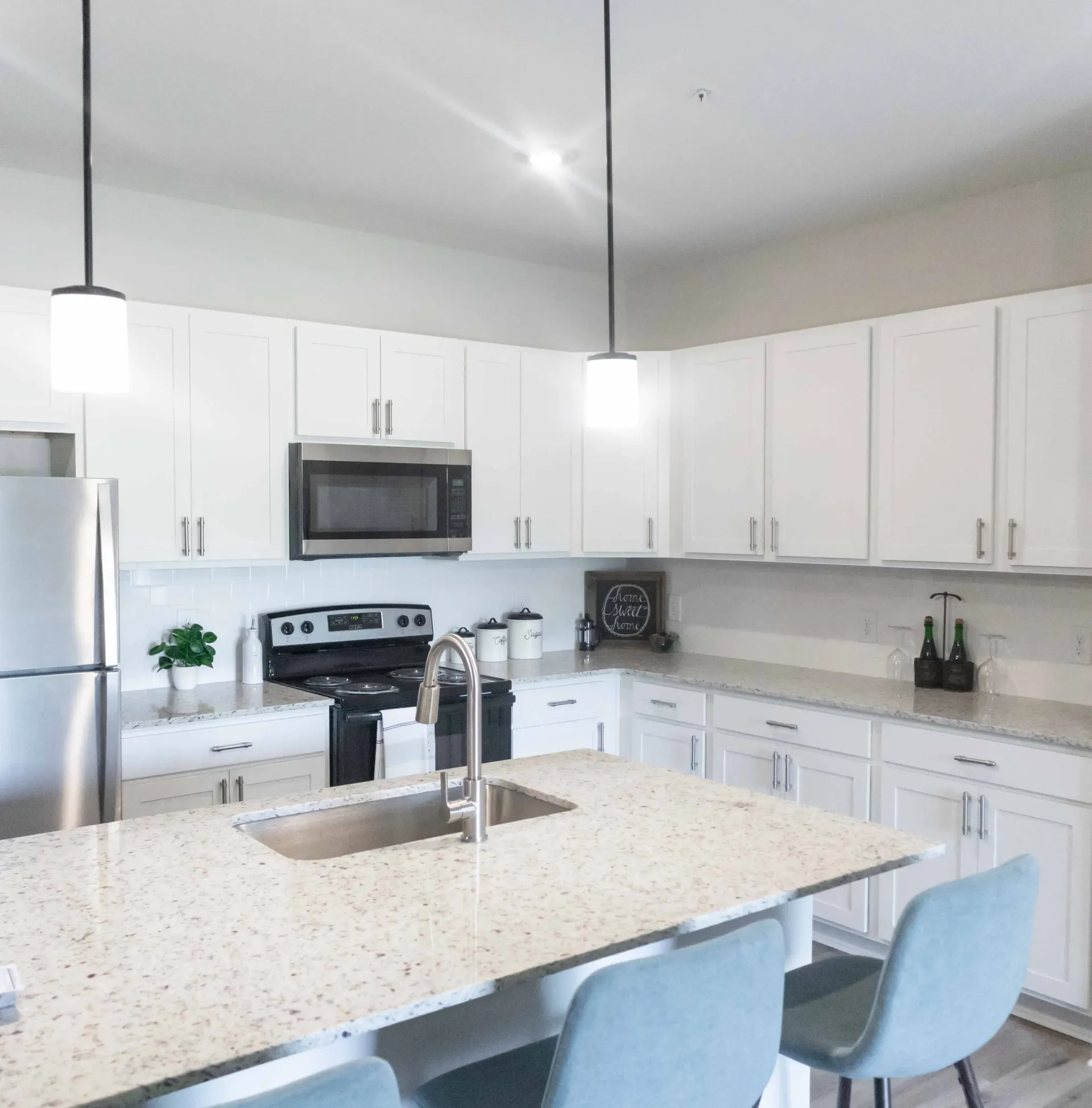 Modern kitchen with white cabinets, stainless steel appliances, and a large island with pendant lights.