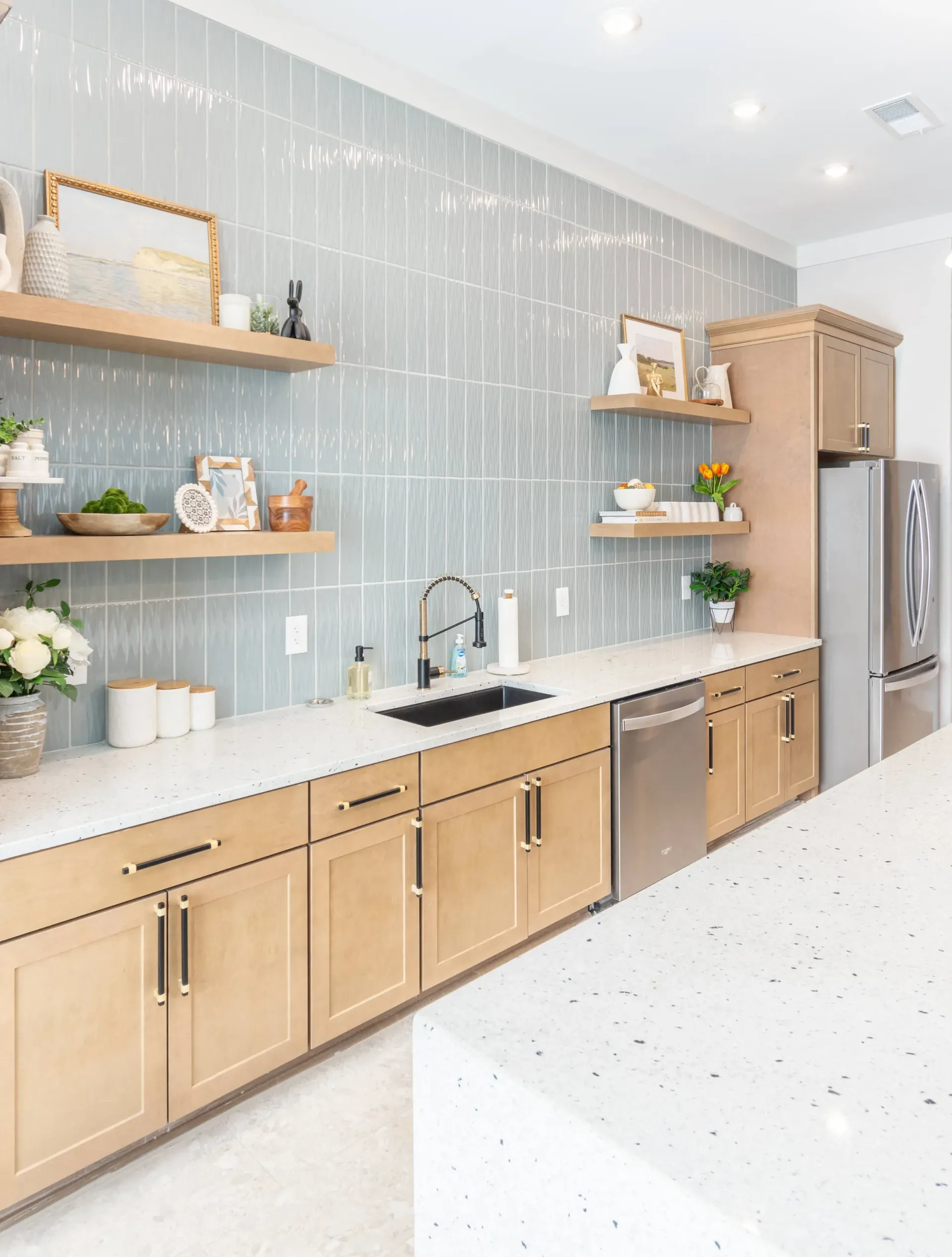 Modern kitchen with light wood cabinets, quartz countertops, and a gray tiled backsplash.