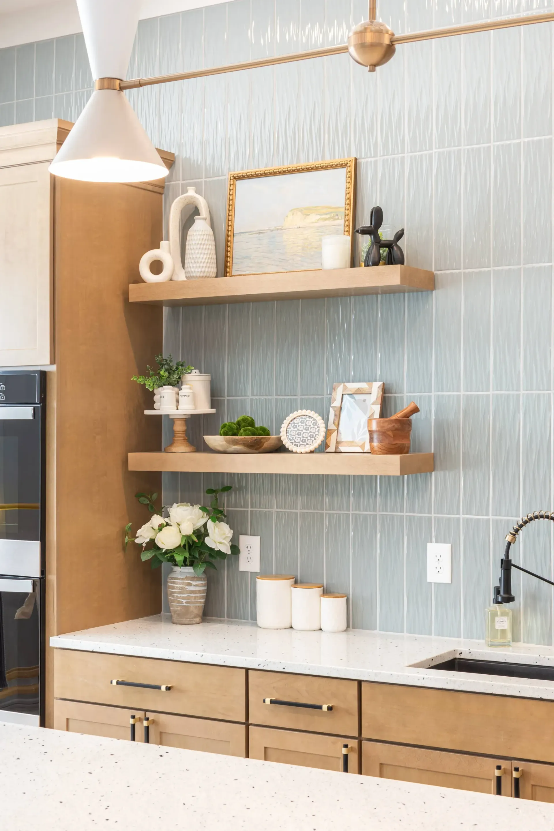 Stylish kitchen with light wood cabinets, white speckled countertops, and a pale blue textured backsplash.