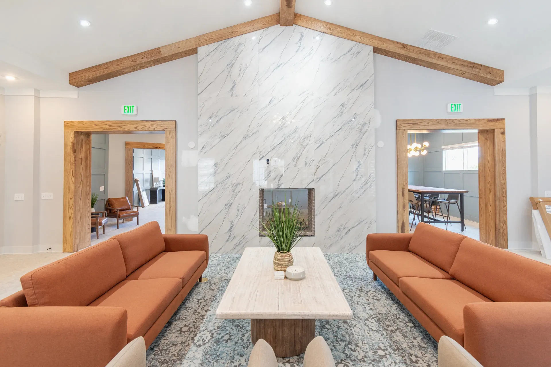 Modern community lounge with two orange sofas facing a marble fireplace and a light wood coffee table.