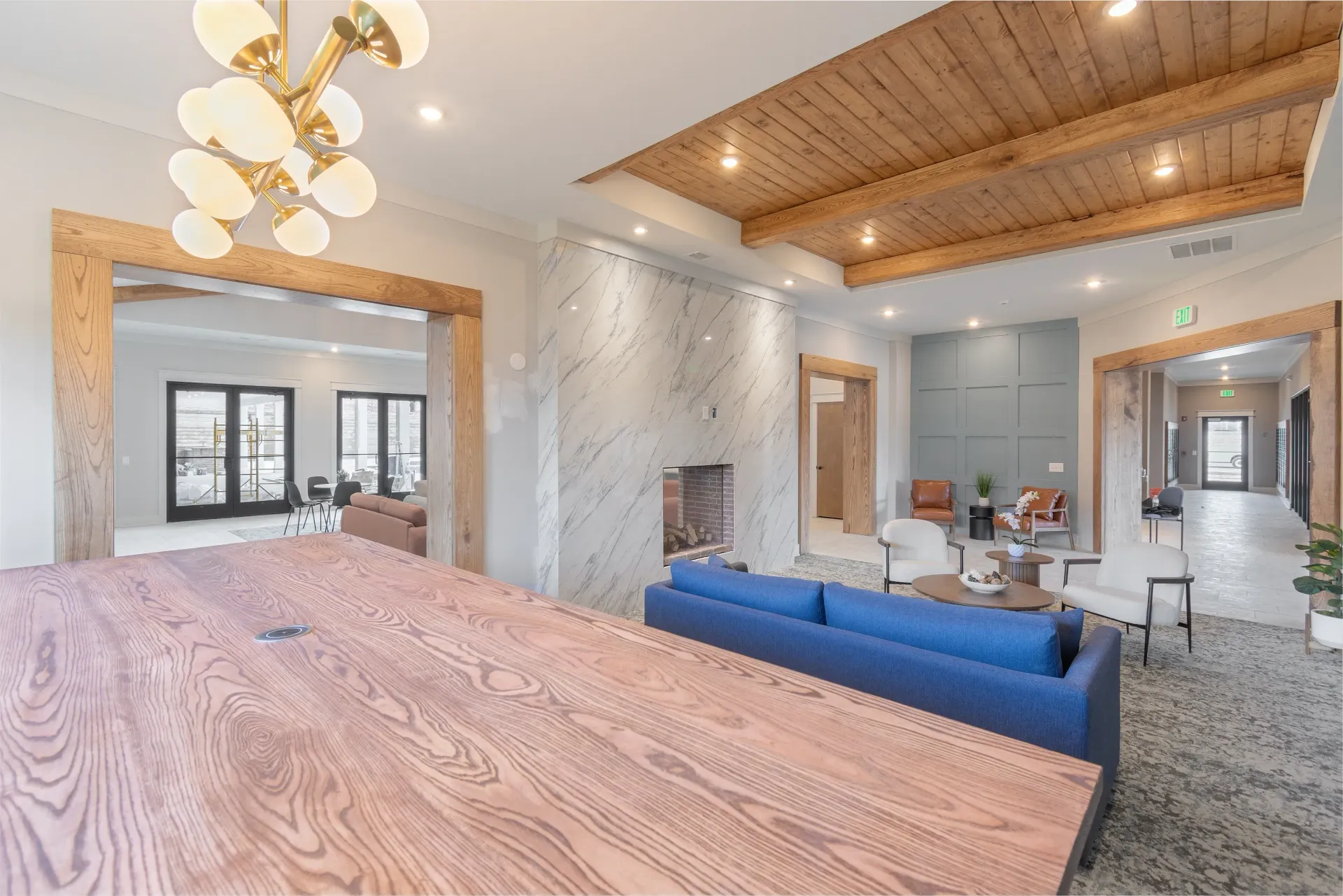 Modern lounge area with a large wooden table, blue sofas, and a marble fireplace.