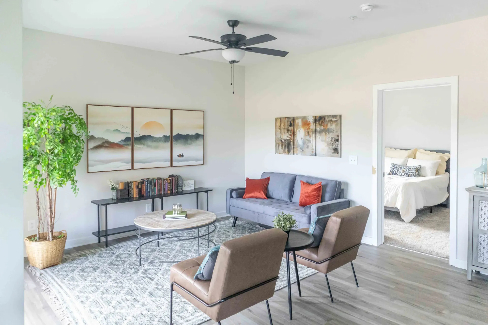 Living room with gray sofa, two armchairs, coffee table, and a view into a bedroom.