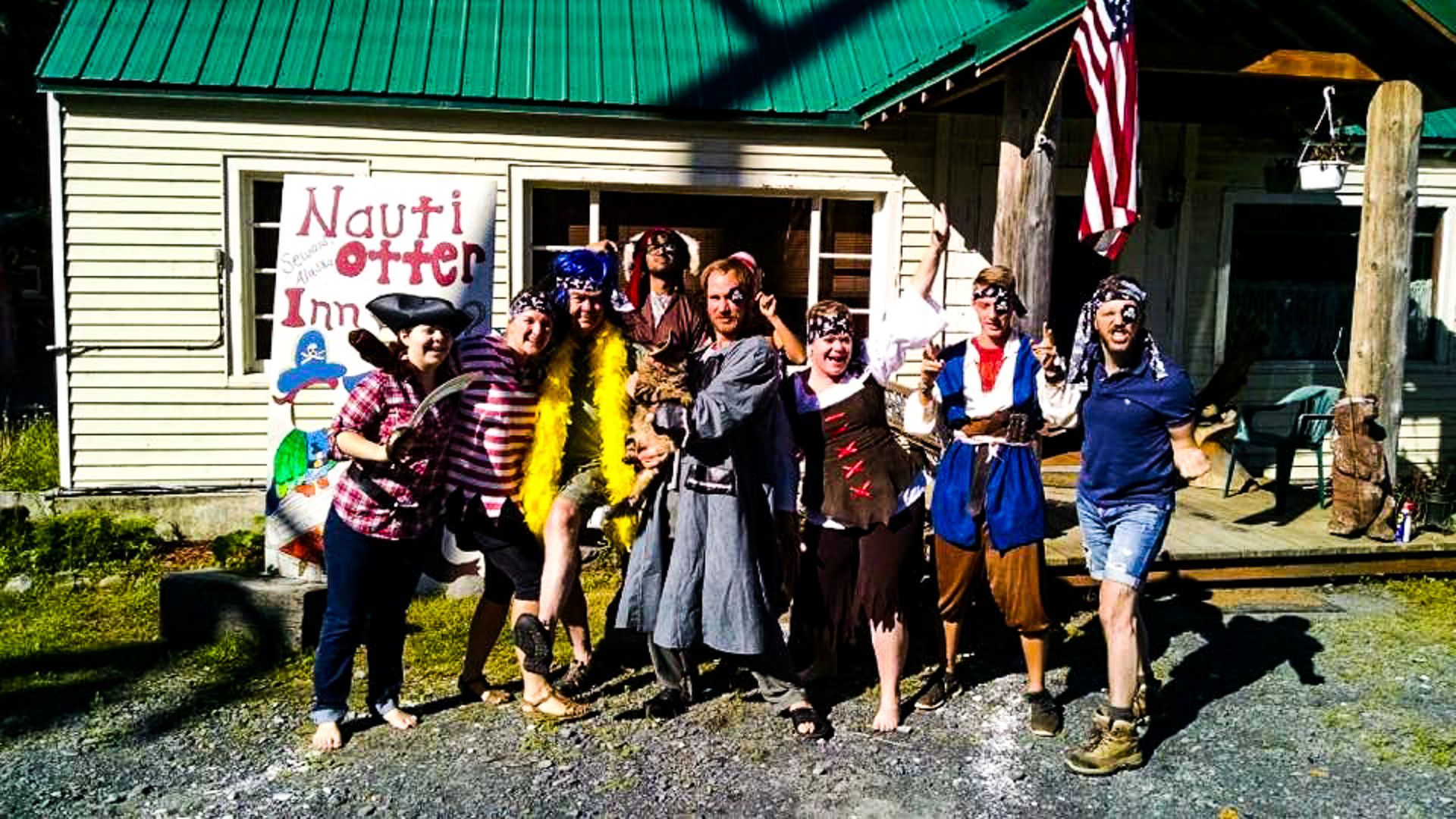 Group of people in pirate costumes posing in front of a building with an American flag.