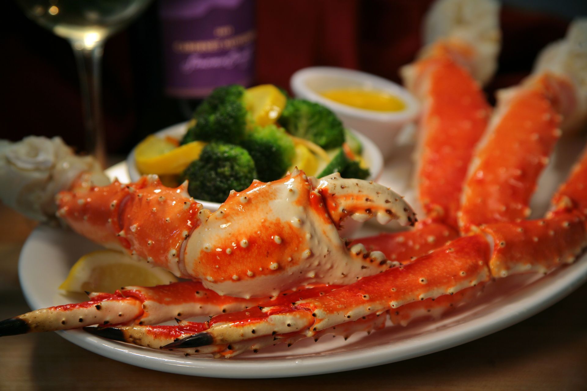 King crab legs with broccoli, squash, melted butter, and wine on a white plate.