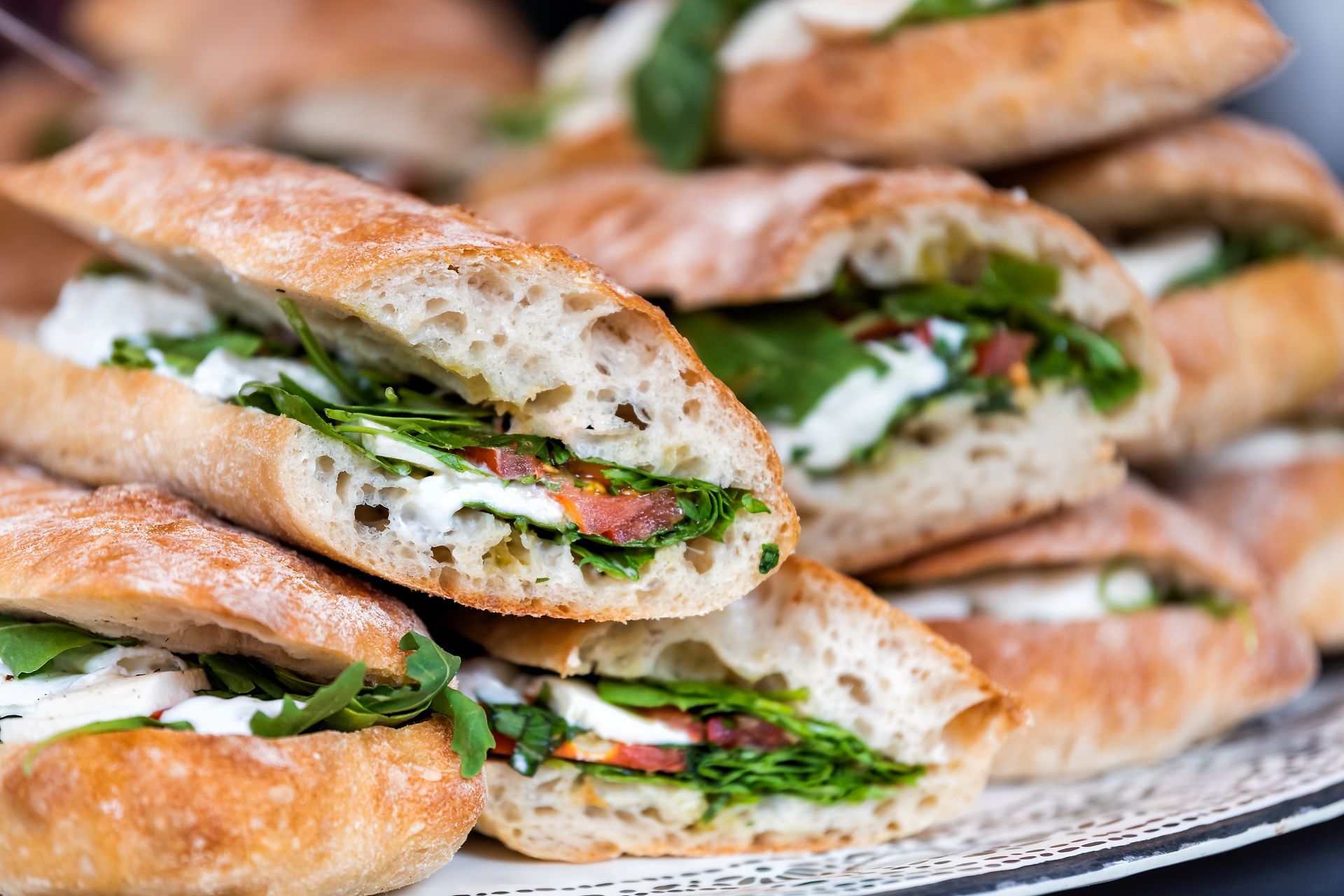 A platter piled high with fresh ciabatta sandwiches filled with arugula, sliced tomatoes, and creamy mozzarella cheese.