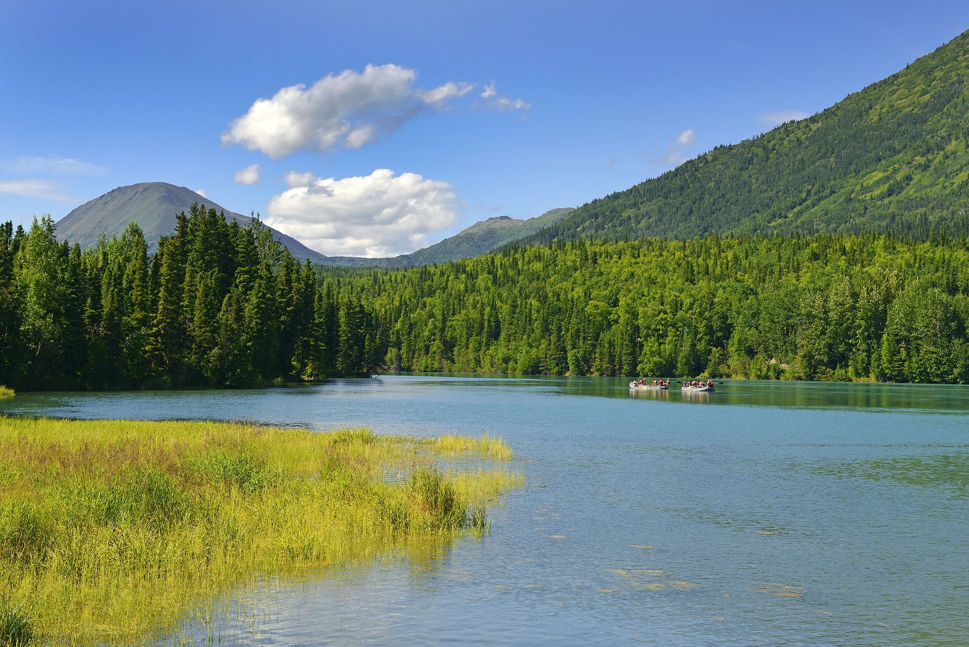 Lake surrounded by green trees and mountains, under a blue sky with clouds.