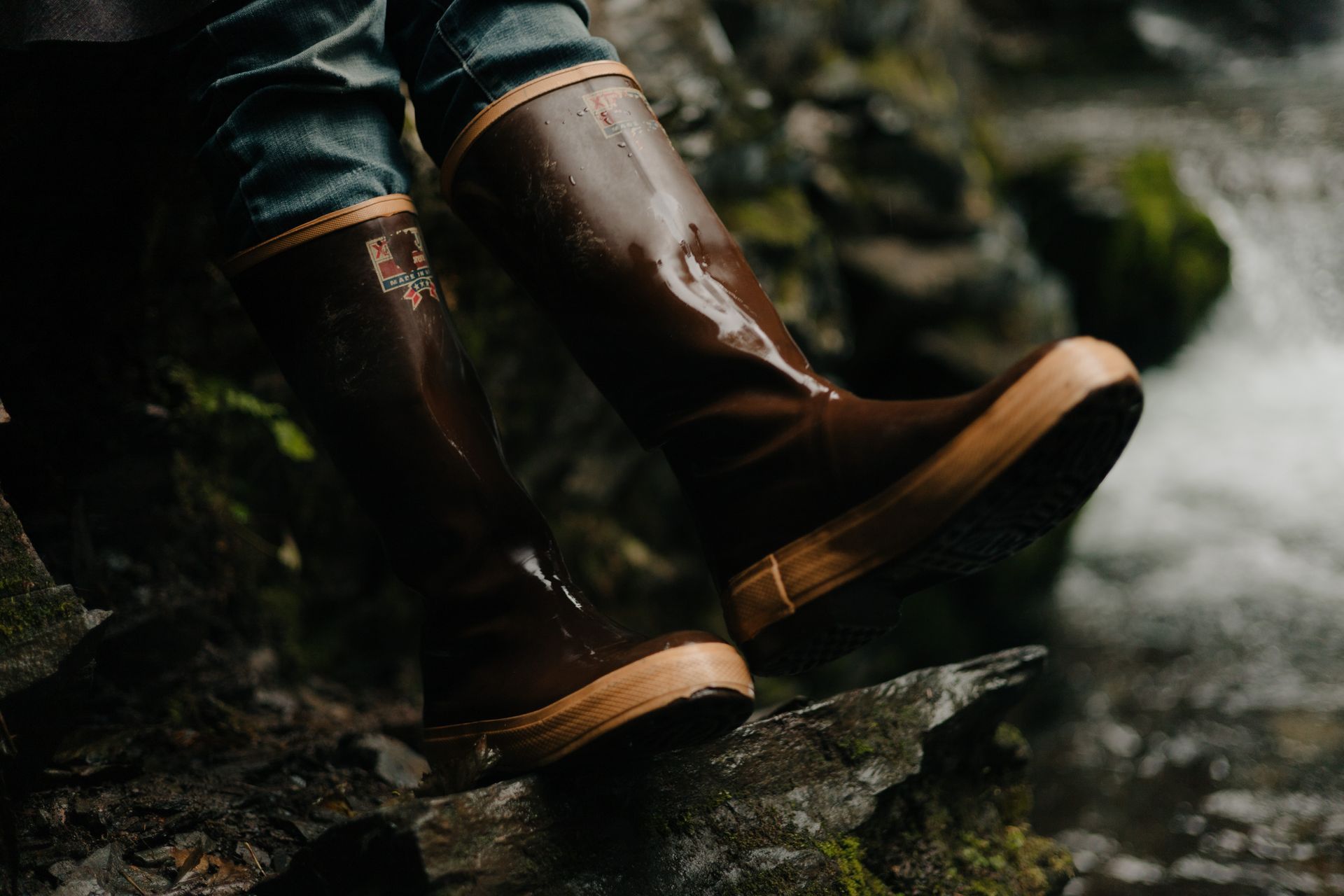 Brown waterproof boots resting on a rock near a stream.