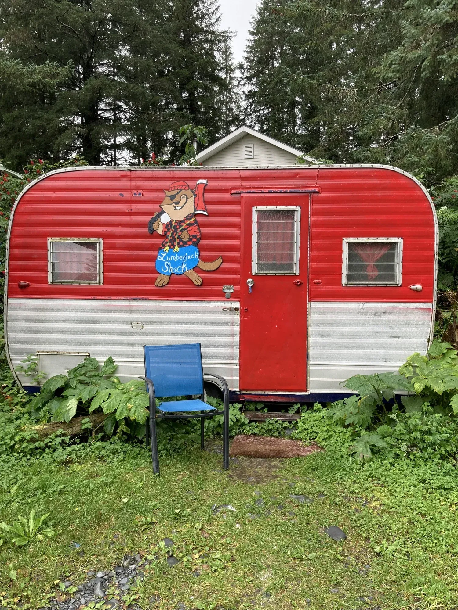 Red and white camper with a cartoon dog, a blue chair sits in front.