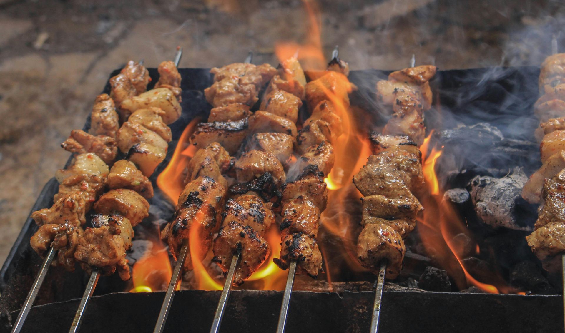Skewers of seasoned meat cooking over an open flame on a charcoal grill.
