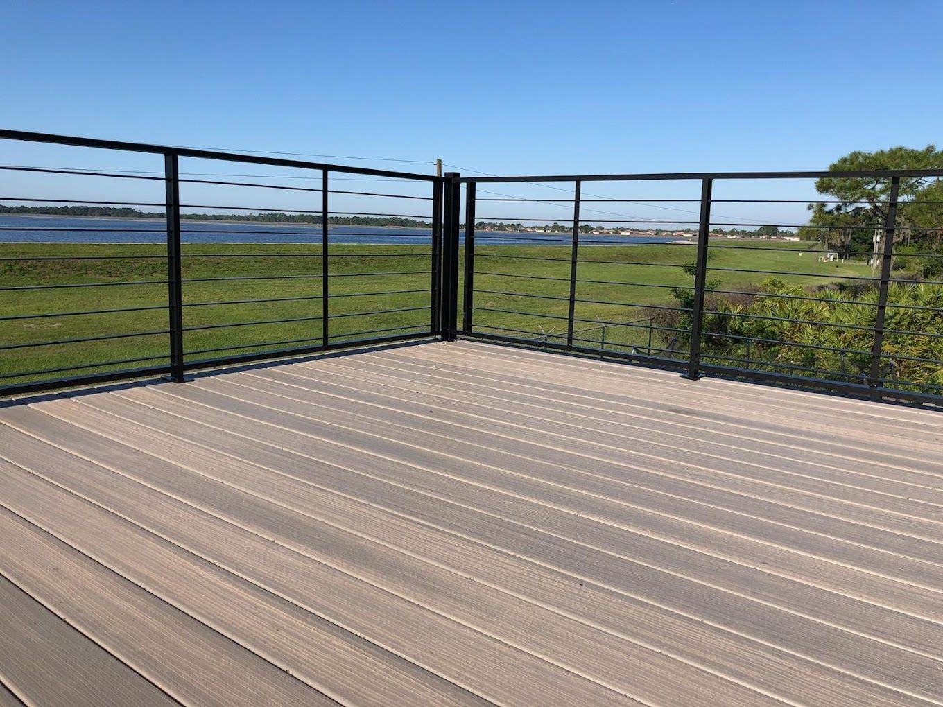 A wooden deck with a black railing overlooking a body of water.