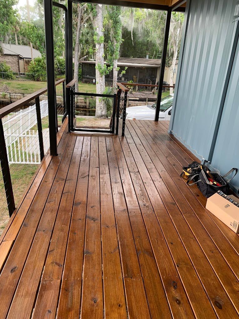 A screened in porch with a wooden deck and a railing.