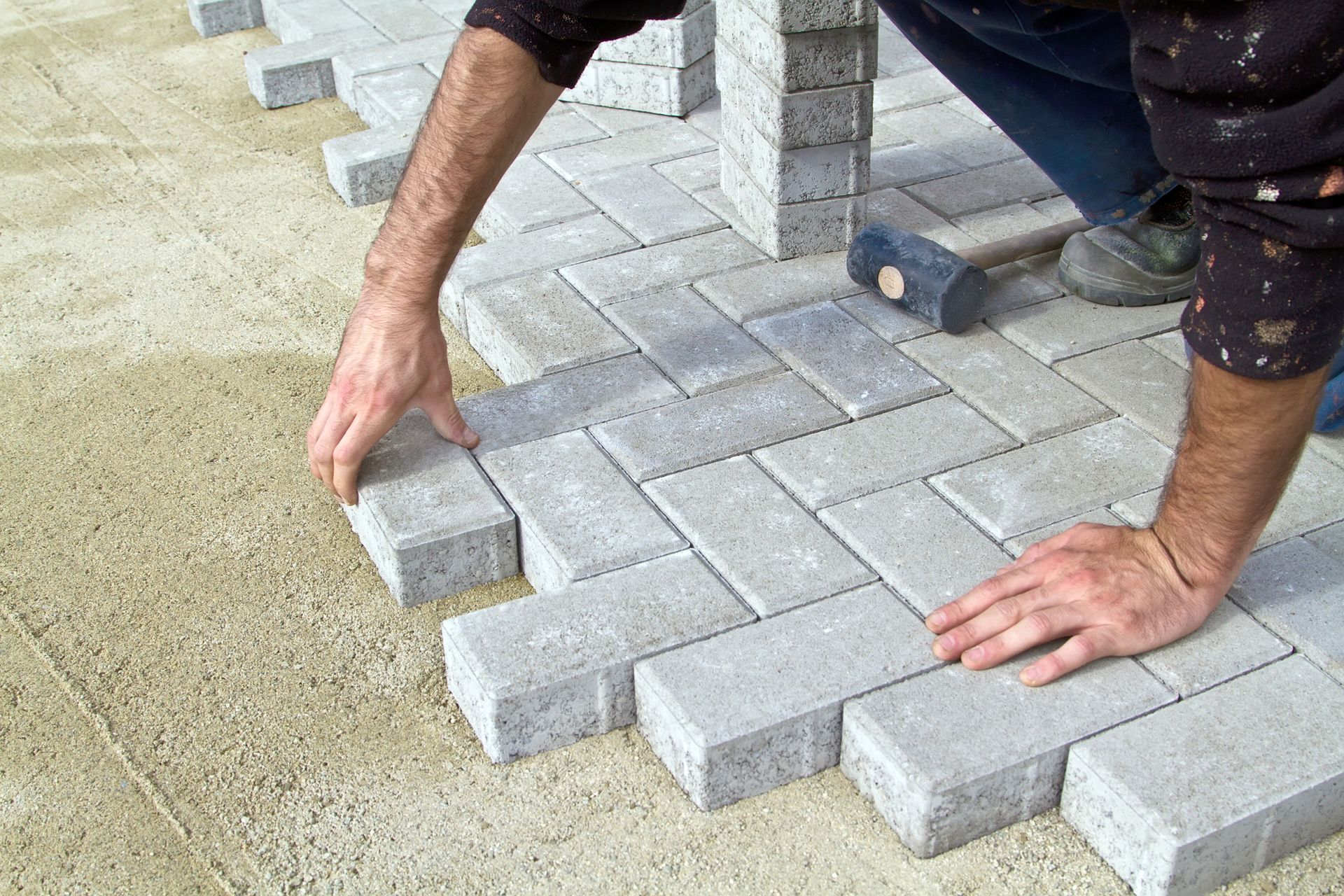 A stone retaining wall borders a patio with a gravel drainage strip, set against a backdrop of trees and trimmed hedges.