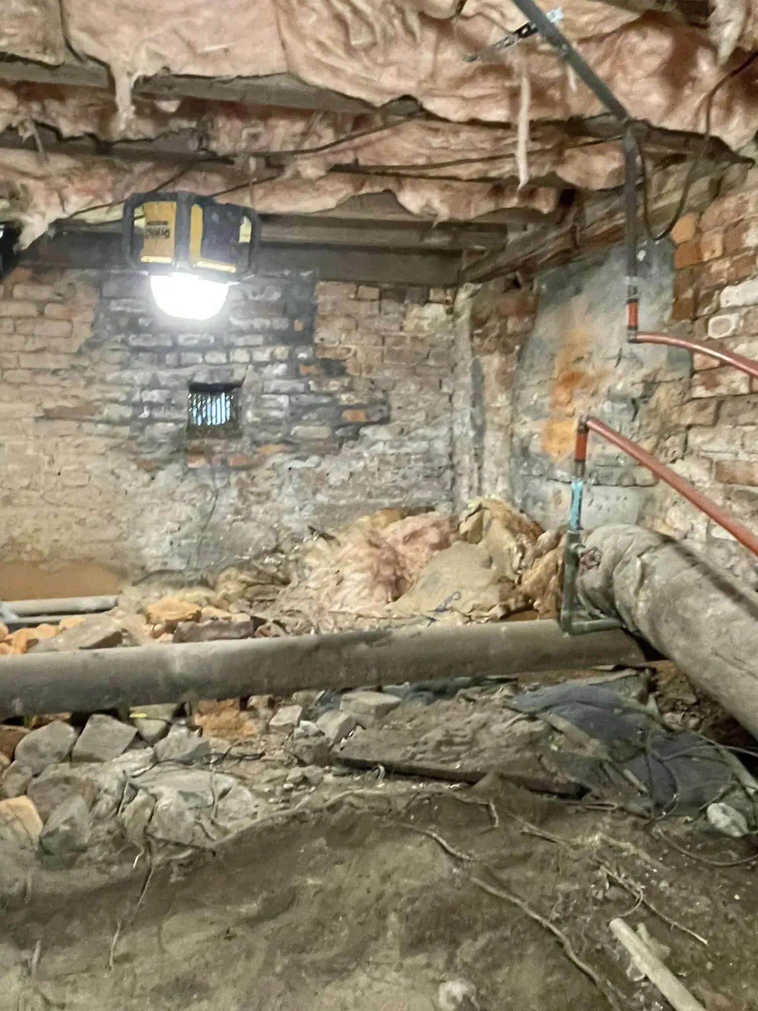 Collapsed basement with debris, exposed beams, stone wall, and a lit hanging work light.