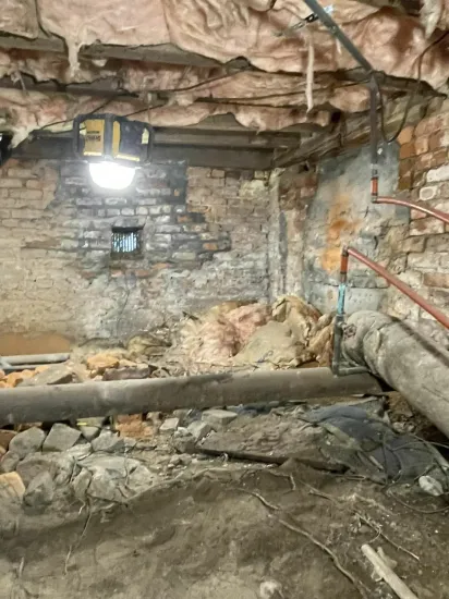 Collapsed basement with debris, exposed beams, stone wall, and a lit hanging work light.