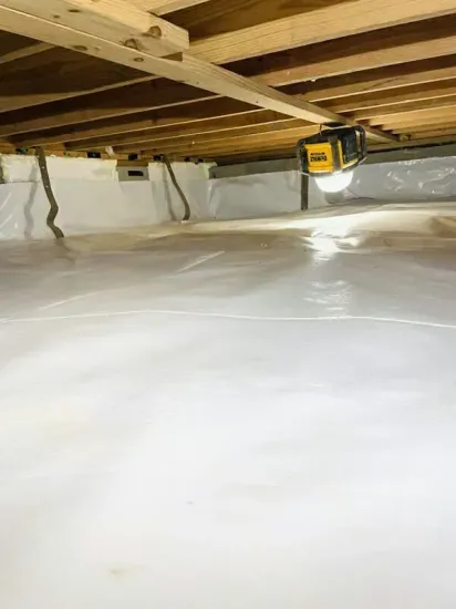 Crawl space with white vapor barrier, exposed wooden joists, and a yellow work light under the floor