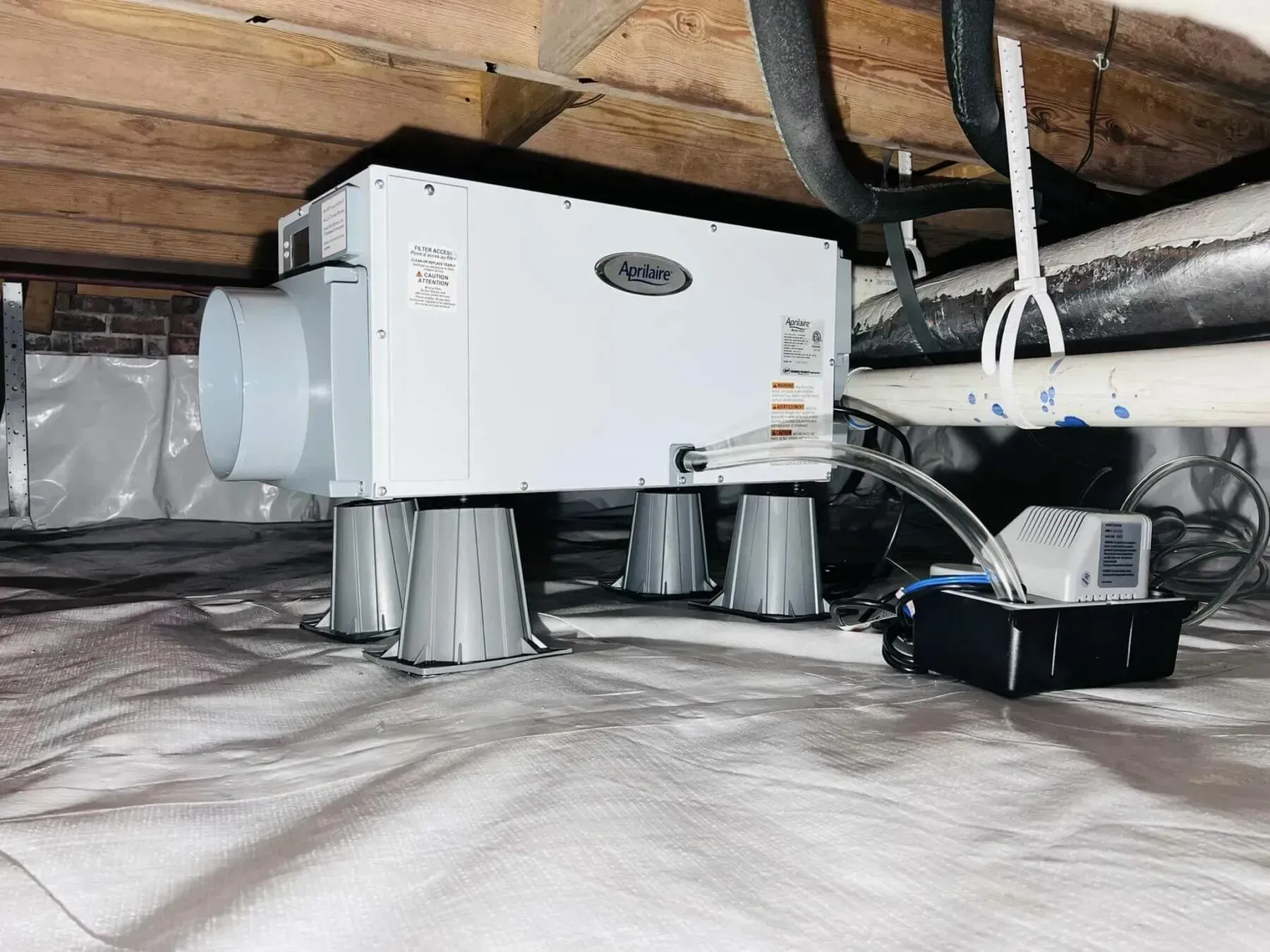 White HVAC unit with ducting and insulated pipes installed in a crawl space under floor joists