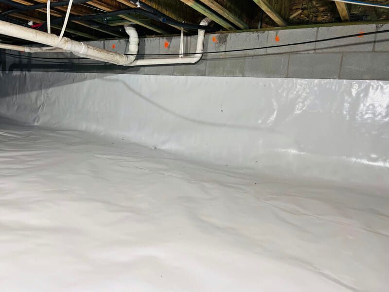Plastic-lined crawlspace under a house with exposed pipes and beams