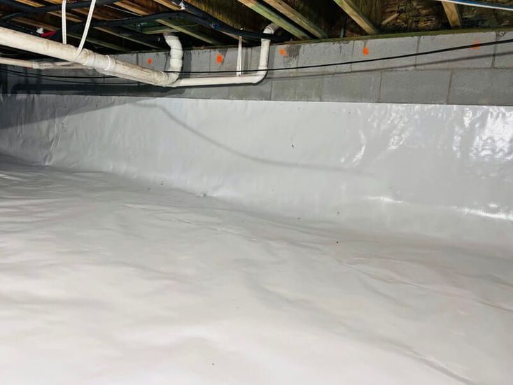 Plastic-lined crawlspace under a house with exposed pipes and beams