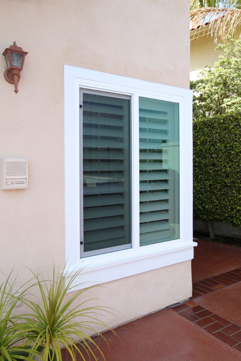A white window with shutters on it is on the side of a house.