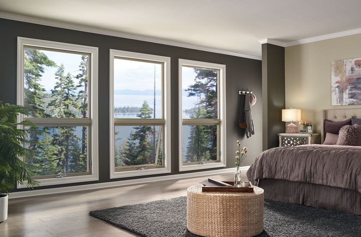 A bedroom with a bed , ottoman , and lots of windows.