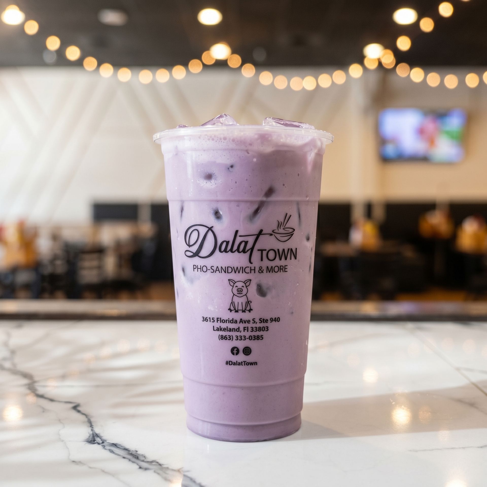 Lavender iced drink in a clear cup on a marble table with blurred cafe lights behind it