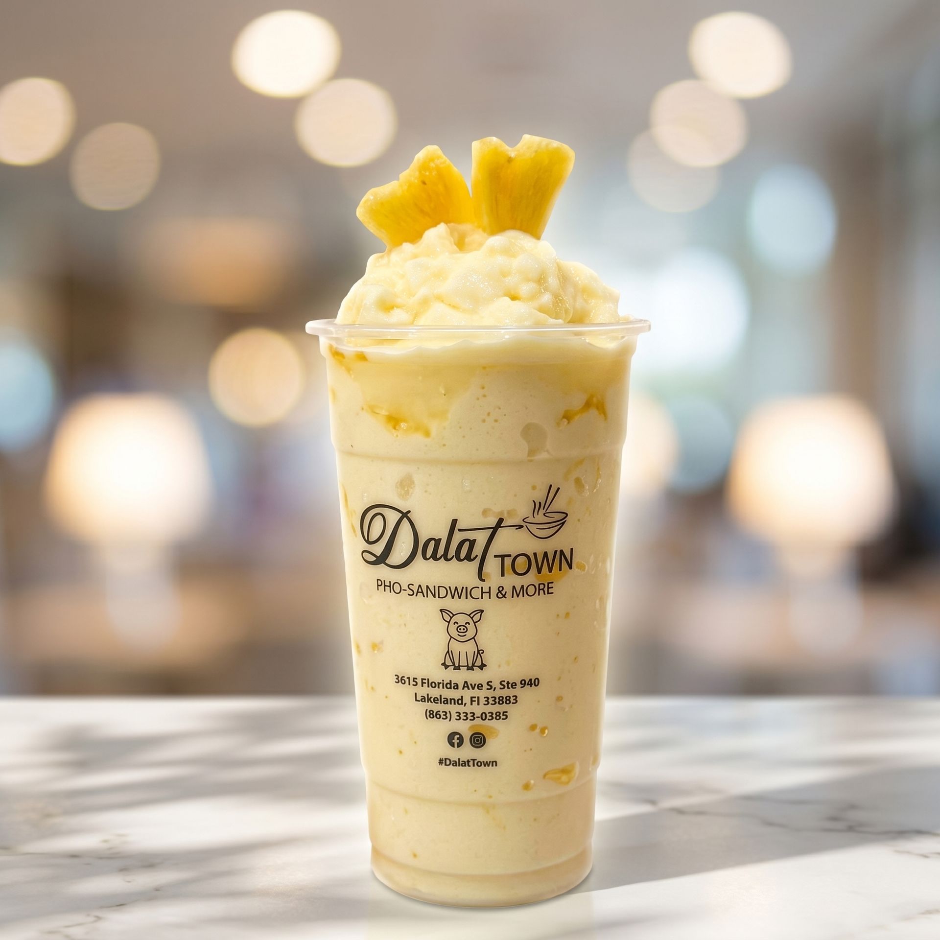 Tall pineapple dessert drink with whipped cream in a clear cup on a table, blurred cafe background
