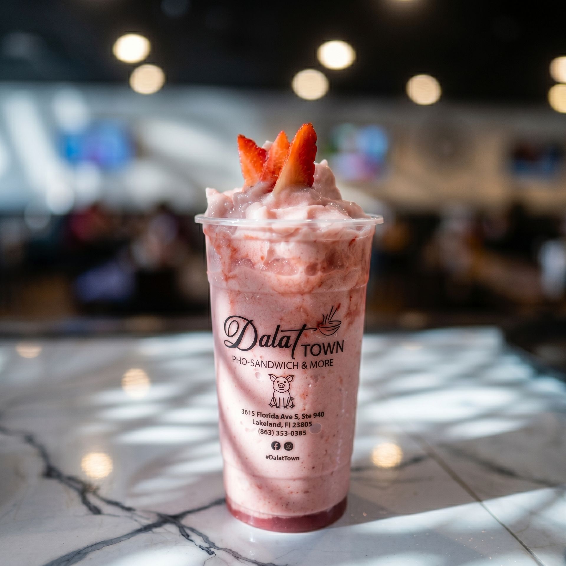 Pink strawberry milkshake topped with whipped cream and strawberry slices on a marble table in a café