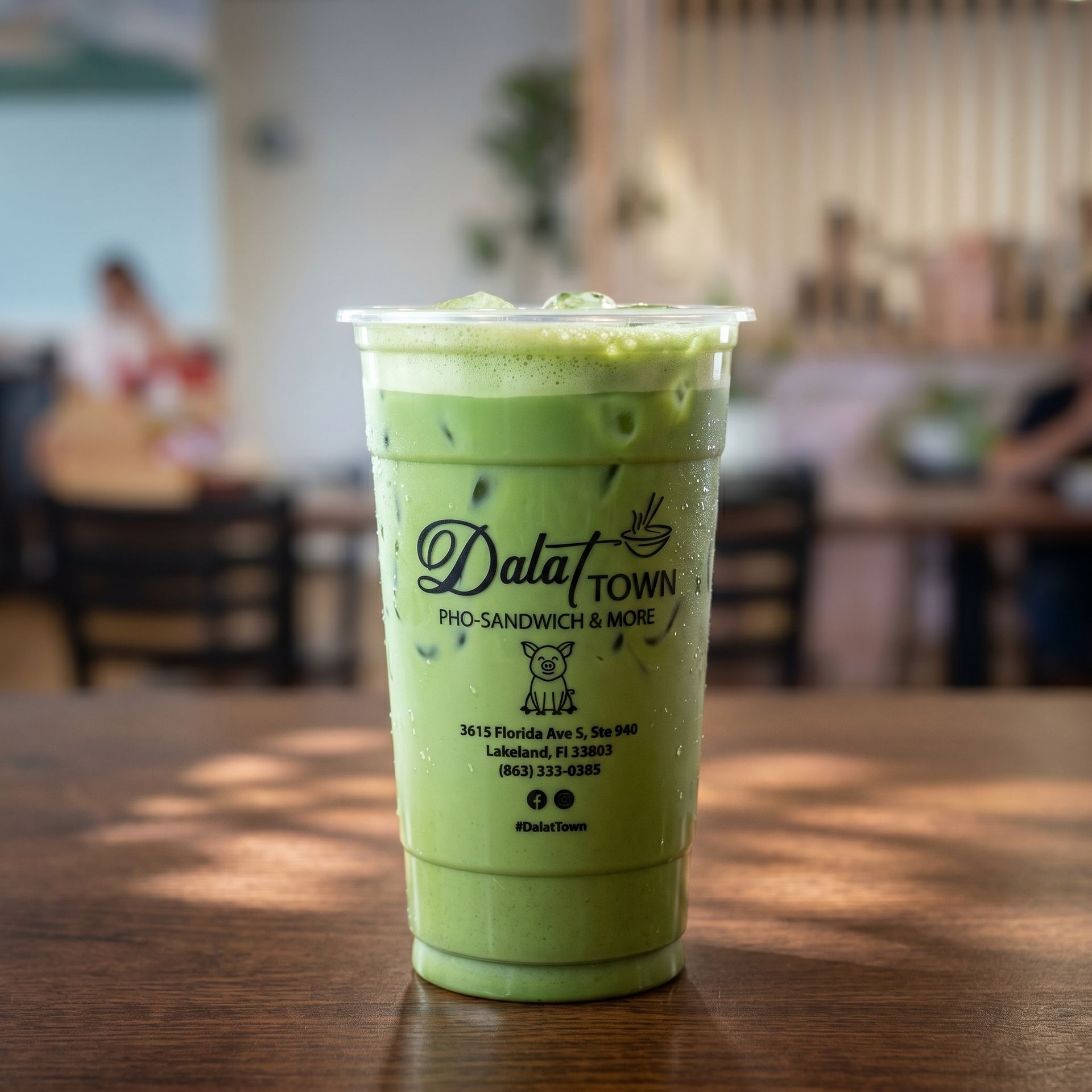 Iced green latte in a clear plastic cup on a wooden table, café background blurred.