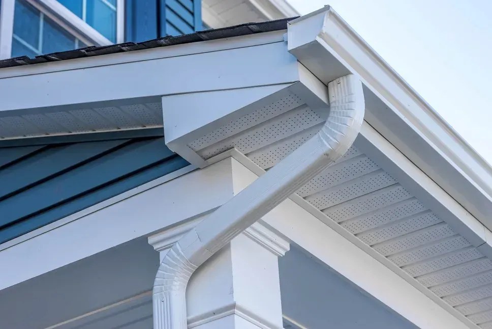 White gutters and downspout on a blue and white house, angled view.