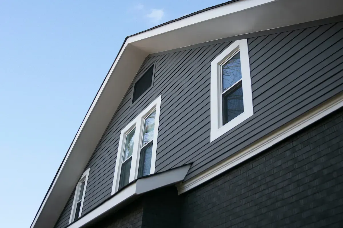 Dark grey house with white trim, multiple windows under a blue sky.