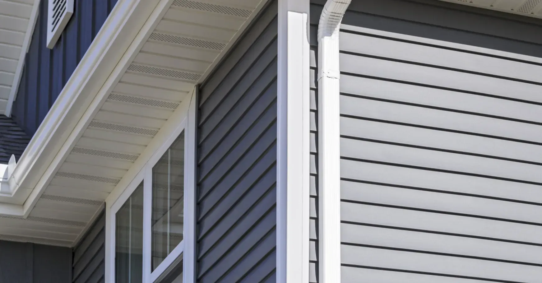 Exterior corner of a house with gray siding and white trim.