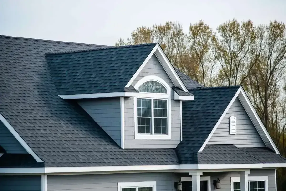 Gray house with dark roof, dormer window, and trees in background.