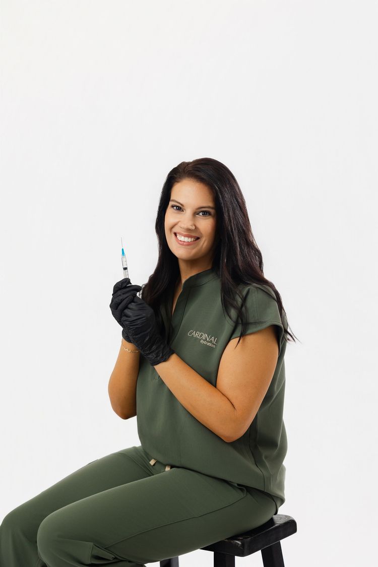 Person in green scrubs and black gloves holding a syringe, seated against a white background.