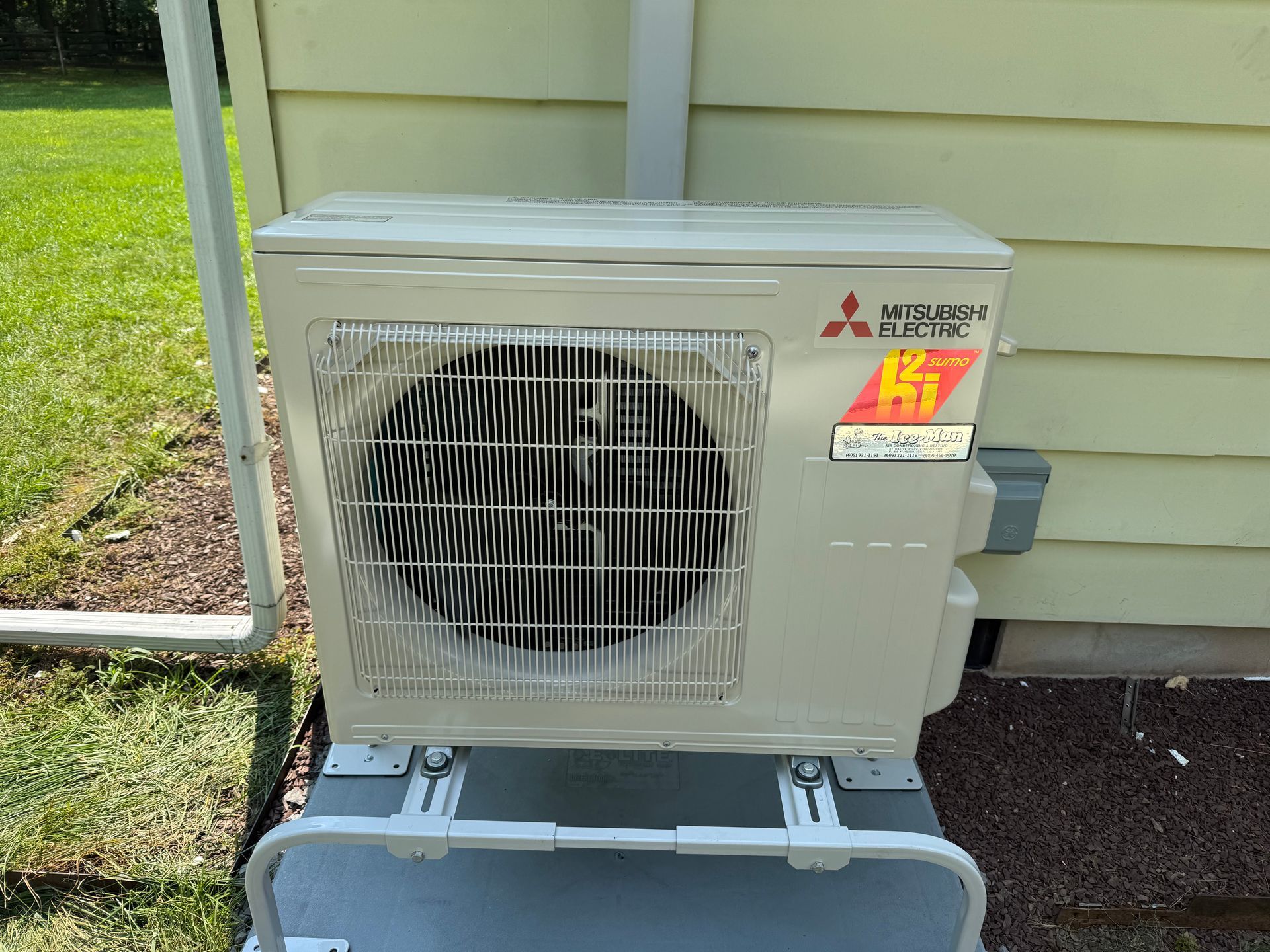 Man standing with arms crossed beside a house’s outdoor air conditioner unit and landscaped yard