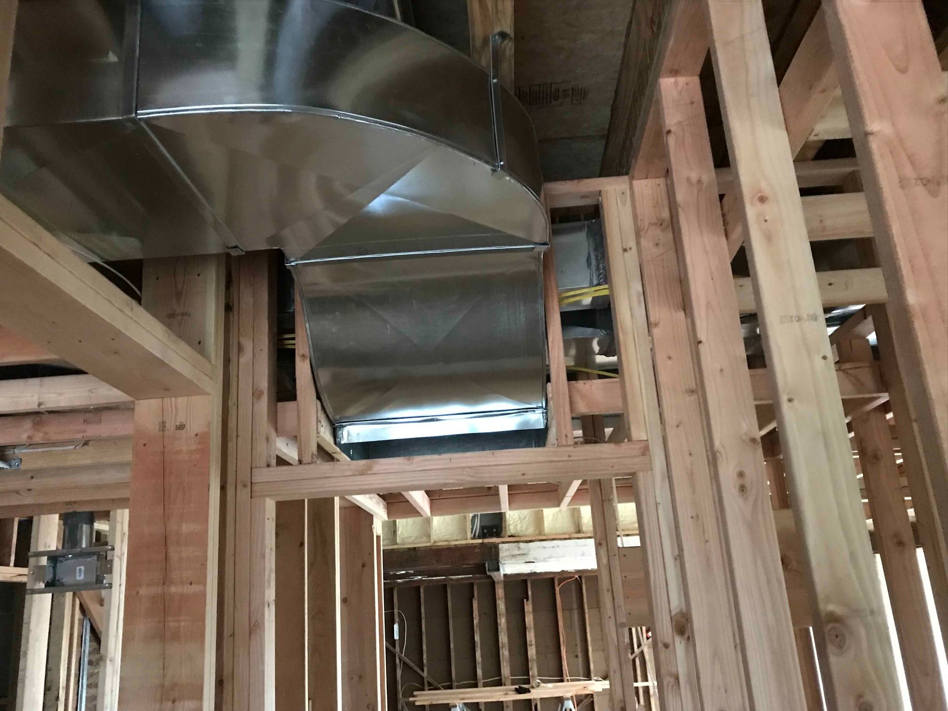 Interior of a house under construction with exposed wooden framing and silver HVAC ducts overhead