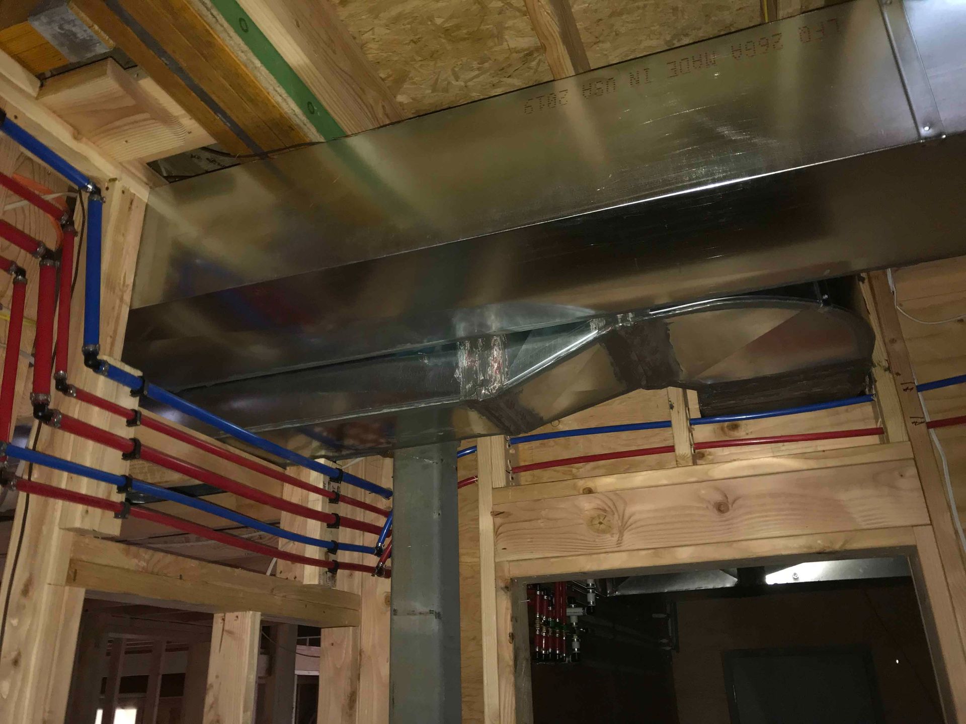 Exposed ceiling with metal HVAC ducts and red-blue utility pipes in a partially finished room