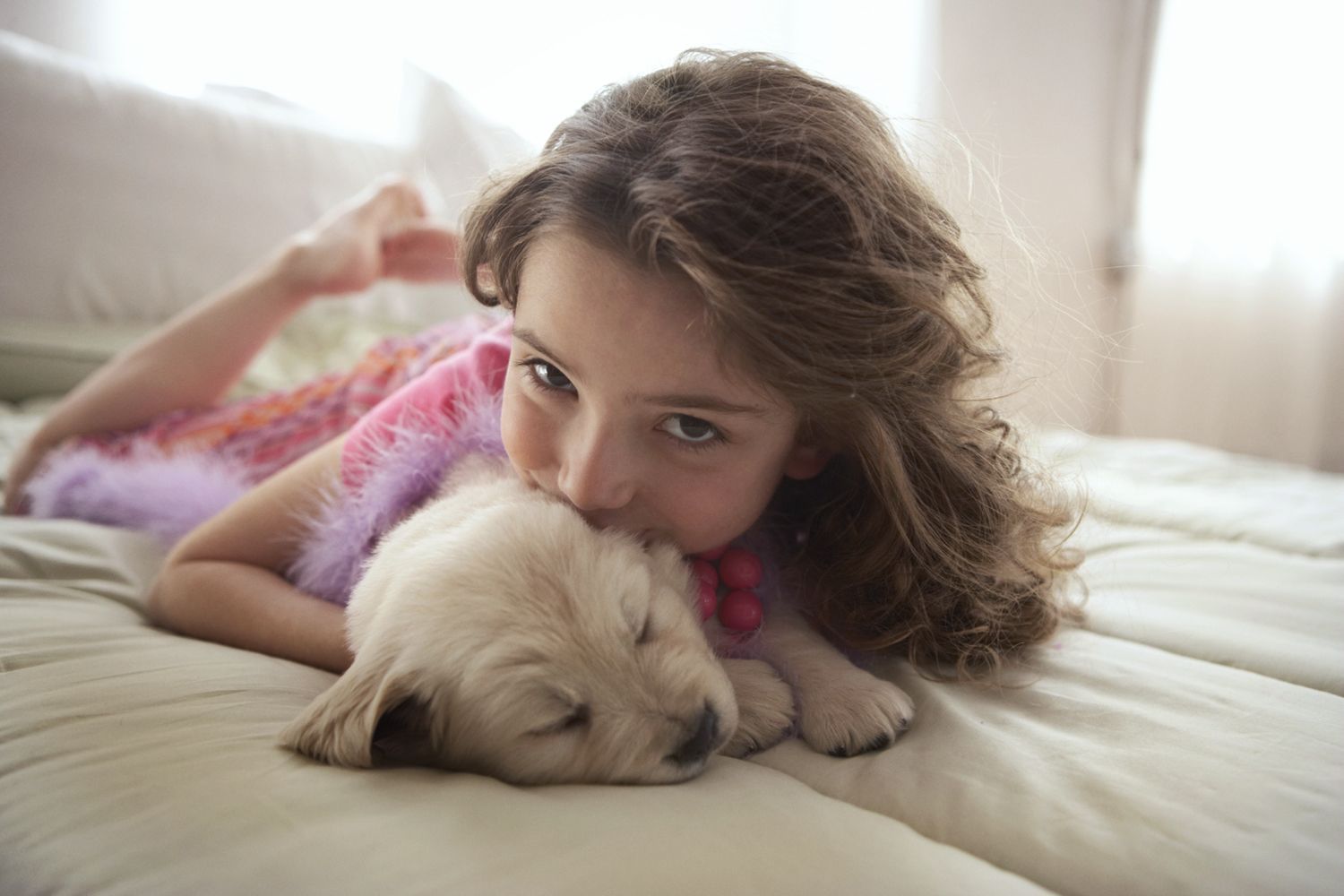 Girl cuddling a sleeping puppy on a bed, resting her chin on its head