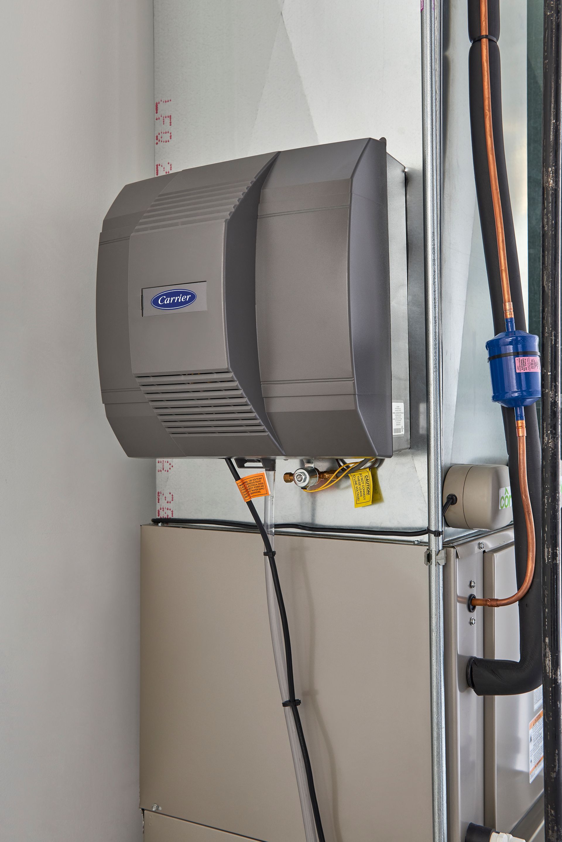Gray wall-mounted HVAC unit with exposed copper pipes and wiring in a utility room