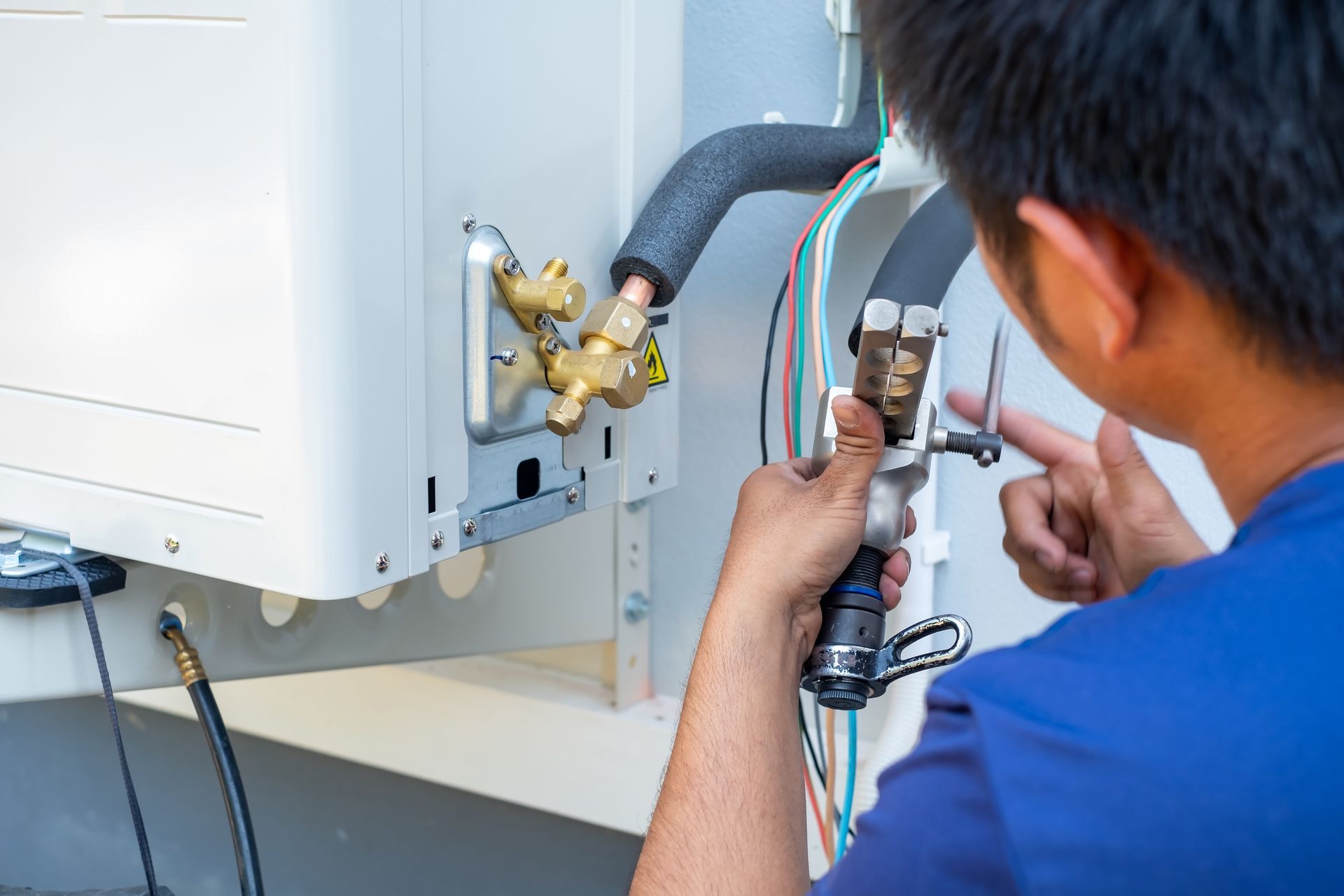 Technician repairing a wall-mounted HVAC unit with tools and exposed wires