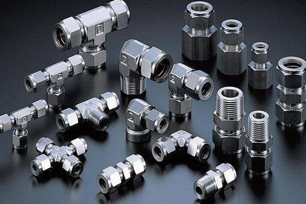 Assorted metal pipe fittings and connectors on a black surface, including tees, elbows, and threaded couplings