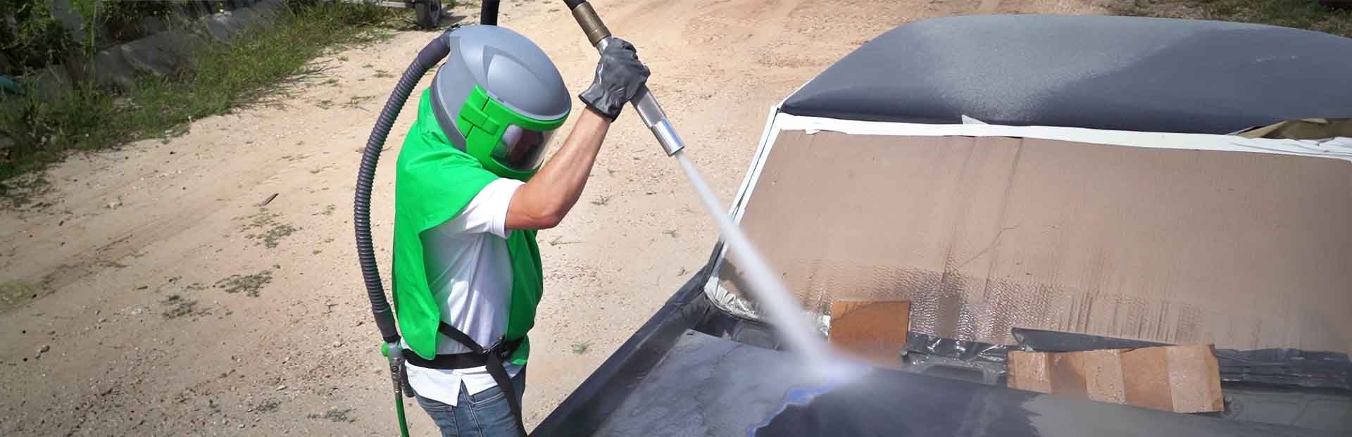 A man wearing a green helmet is sandblasting a car.