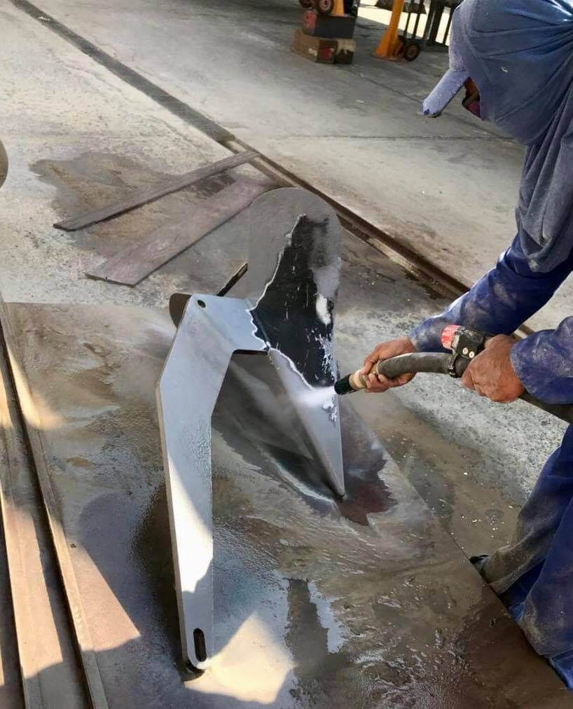 A man is cleaning a piece of metal with a hose.