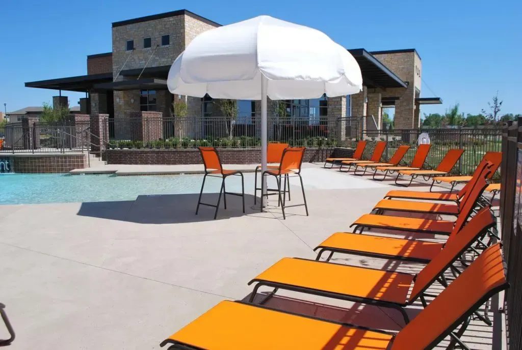 A swimming pool with a white umbrella and orange lounge chairs