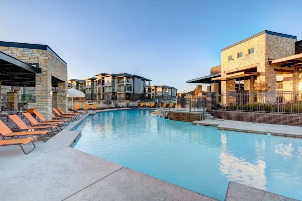 A large swimming pool surrounded by chairs and buildings in a resort.